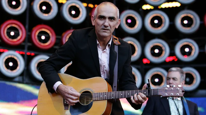 Musician playing an acoustic guitar on stage with circular lights in the background.