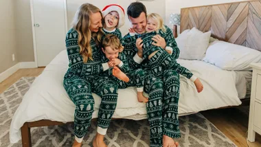 A family of five sitting on a bed. They are all wearing matching green Christmas pyjamas featuring Christmas trees.