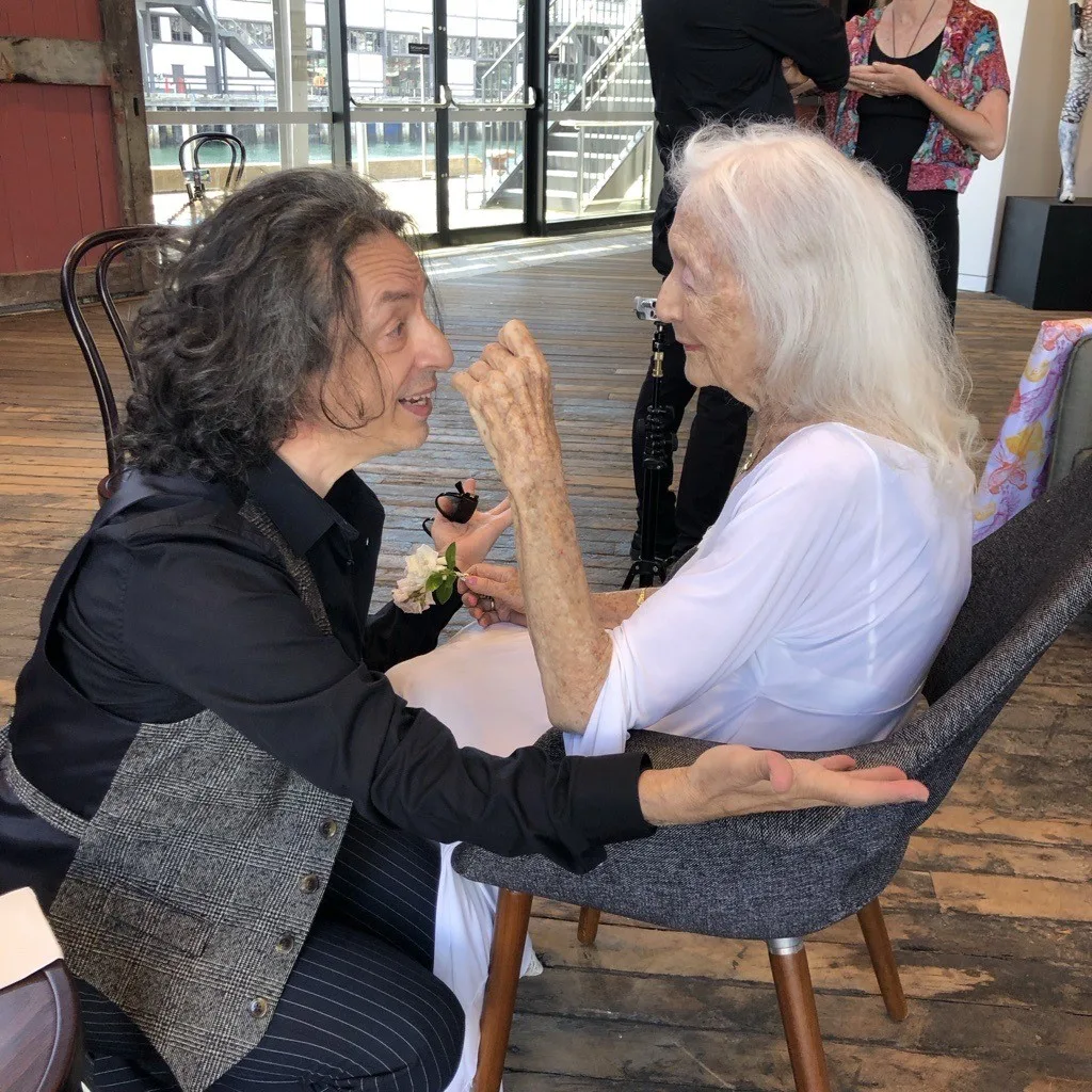 Eileen and Paul Capsis sit together as he sings to her. Eileen holds a white gardenia.