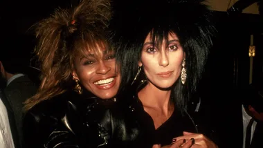 Two women with 1980s hairstyles and leather outfits smiling at a social event.
