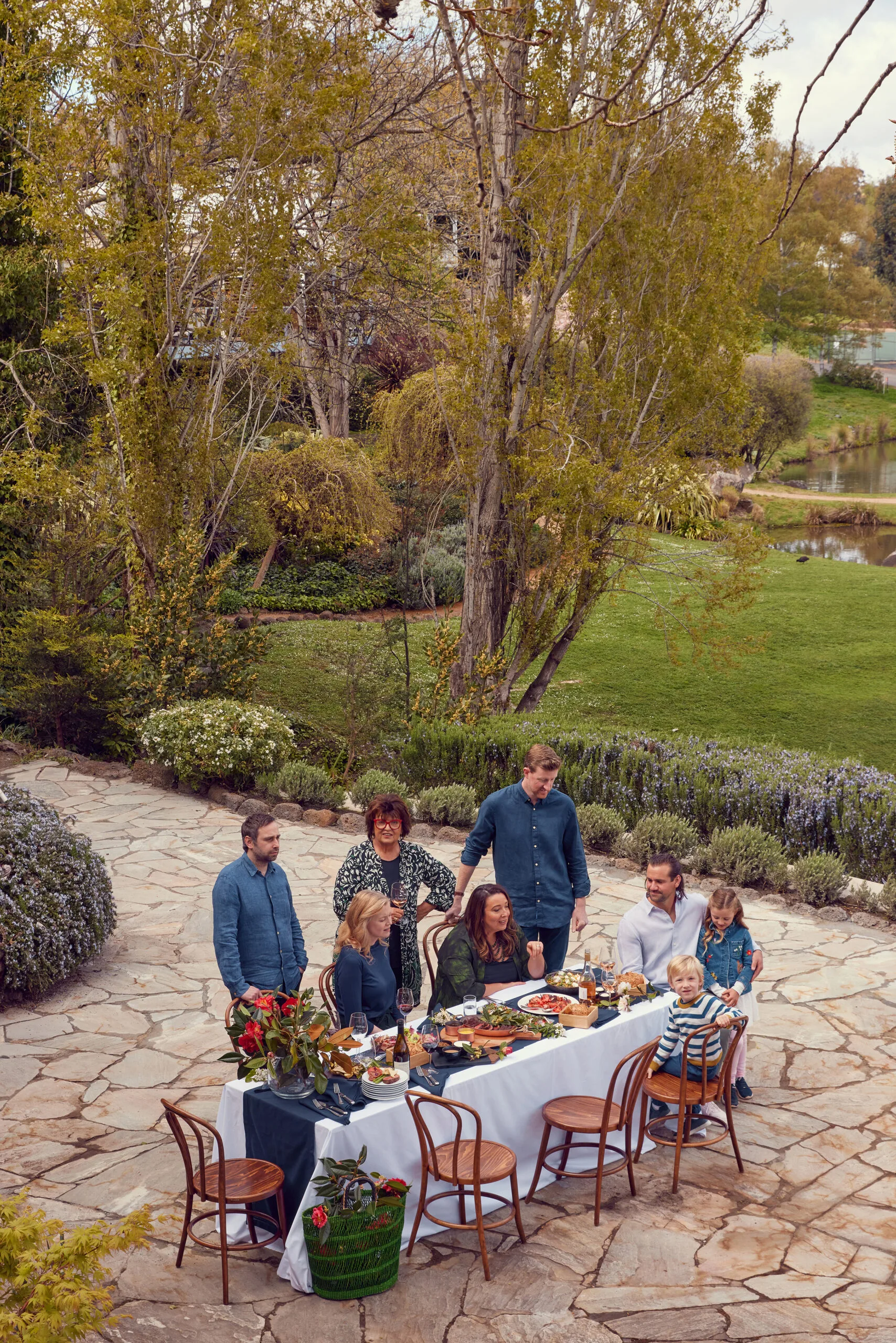 Alla Wolf-Tasker and a group of family and friends sit around an outdoor table laden with food and an arragement of flowers.