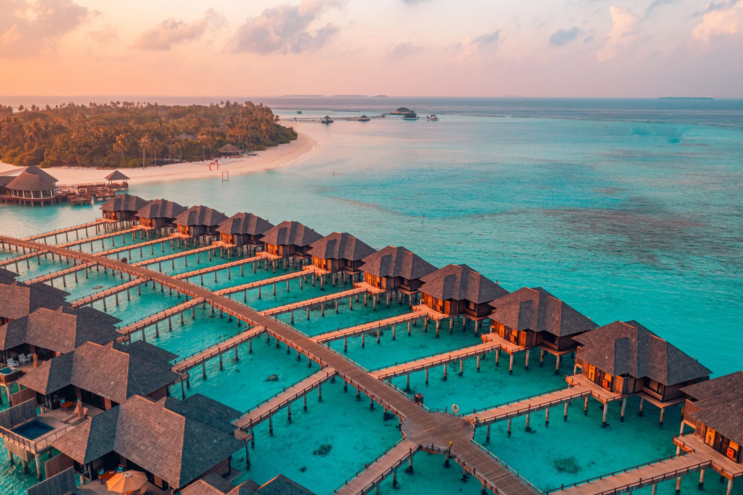Aerial view of a luxury Maldives resort featuring overwater villas stretching into the lagoon at sunset.