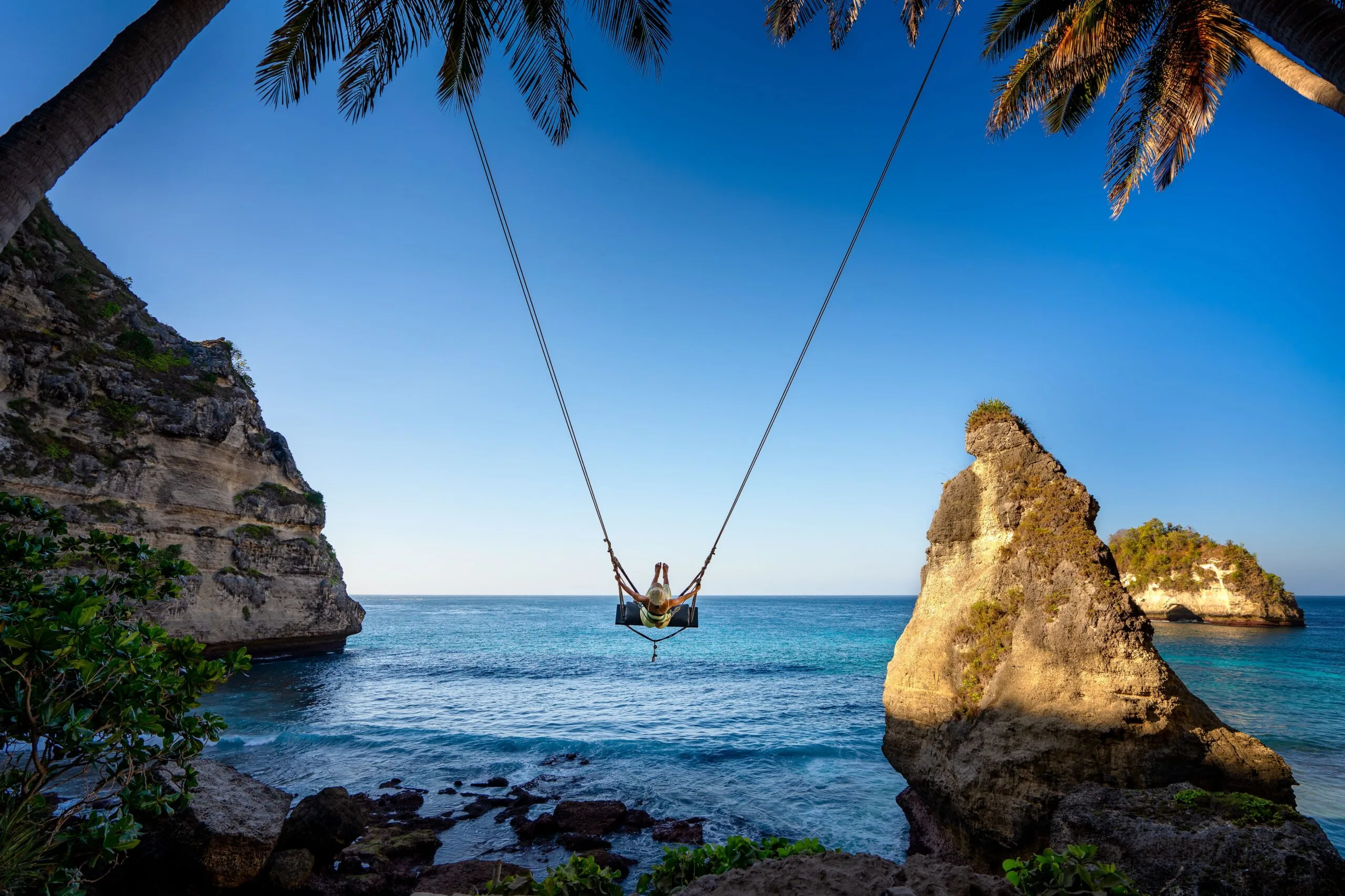 A young woman swinging between two palm trees on a beach in Nusa Penida, Indonesia. Image for the article - best Black Friday flight sales