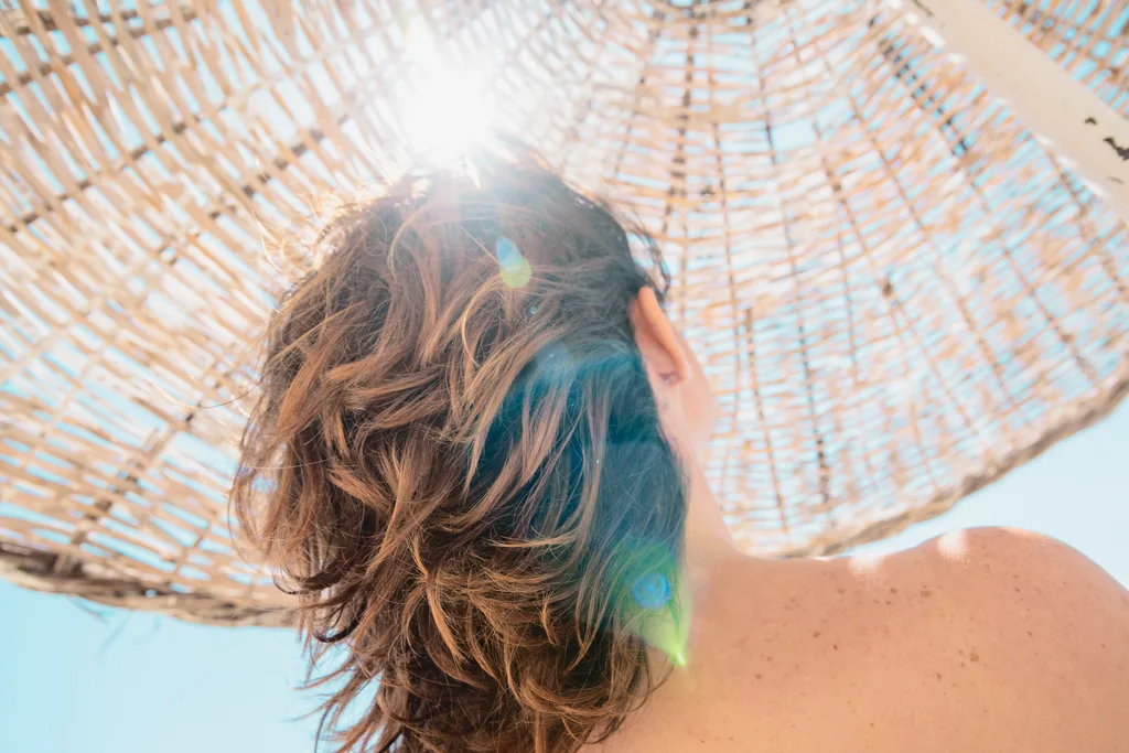 A woman seeking shade at the beach to avoid 'swimmers hair'.