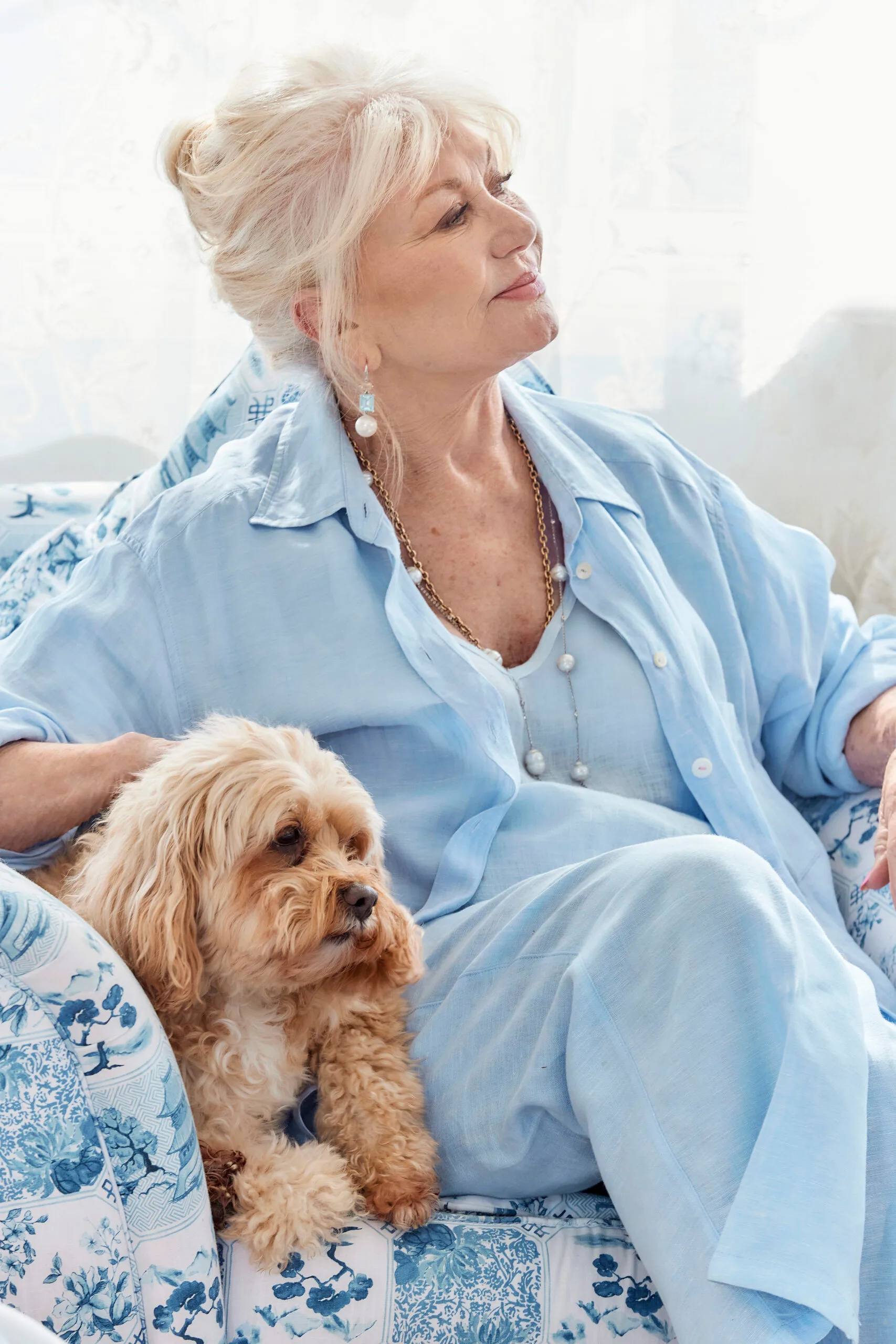 Di Morrissey, a white woman with blonde hair, sits on a couch with a dog.