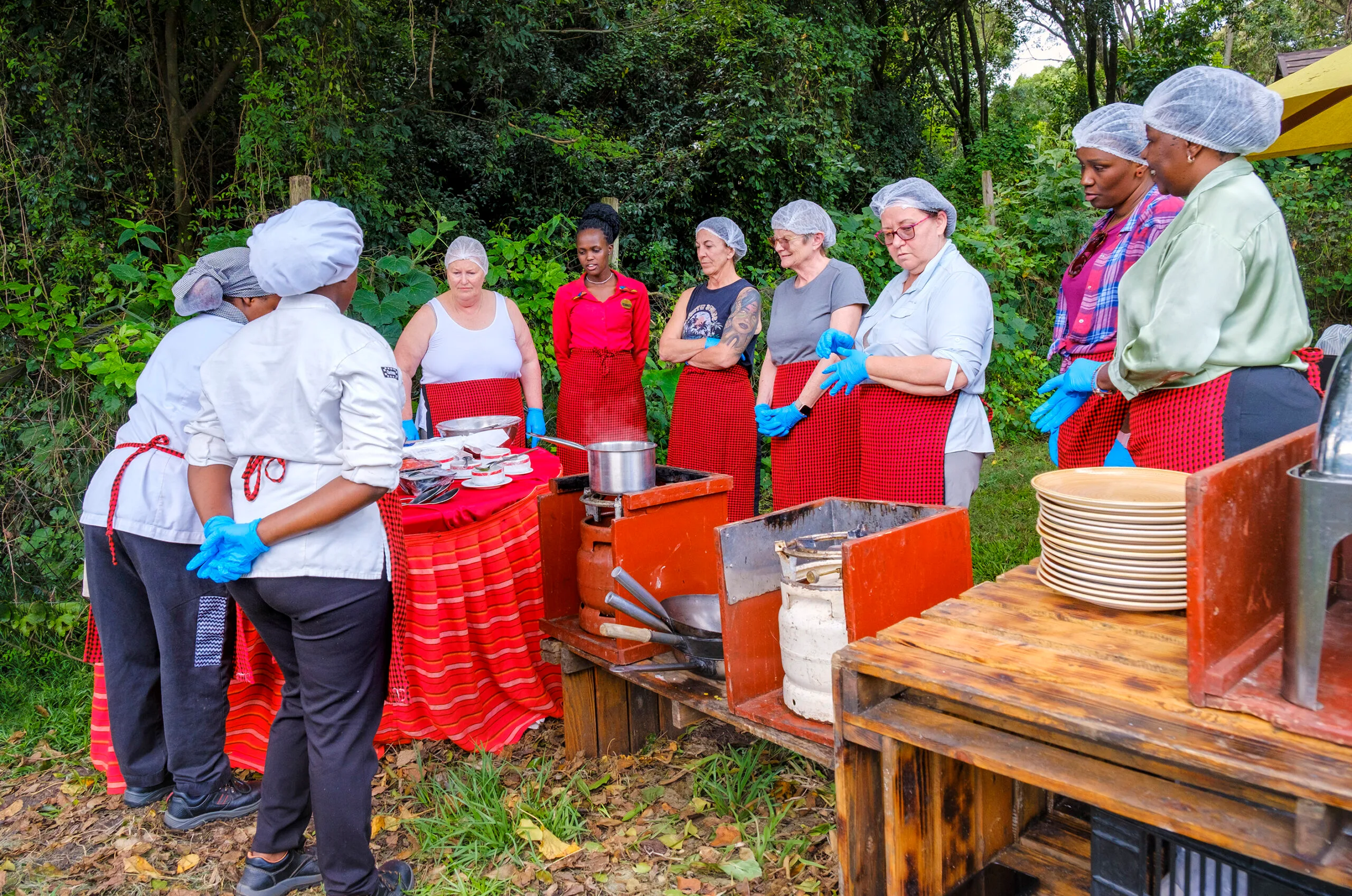 Women-only Kenya tour participants in bright red aprons listen to a cooking teacher.