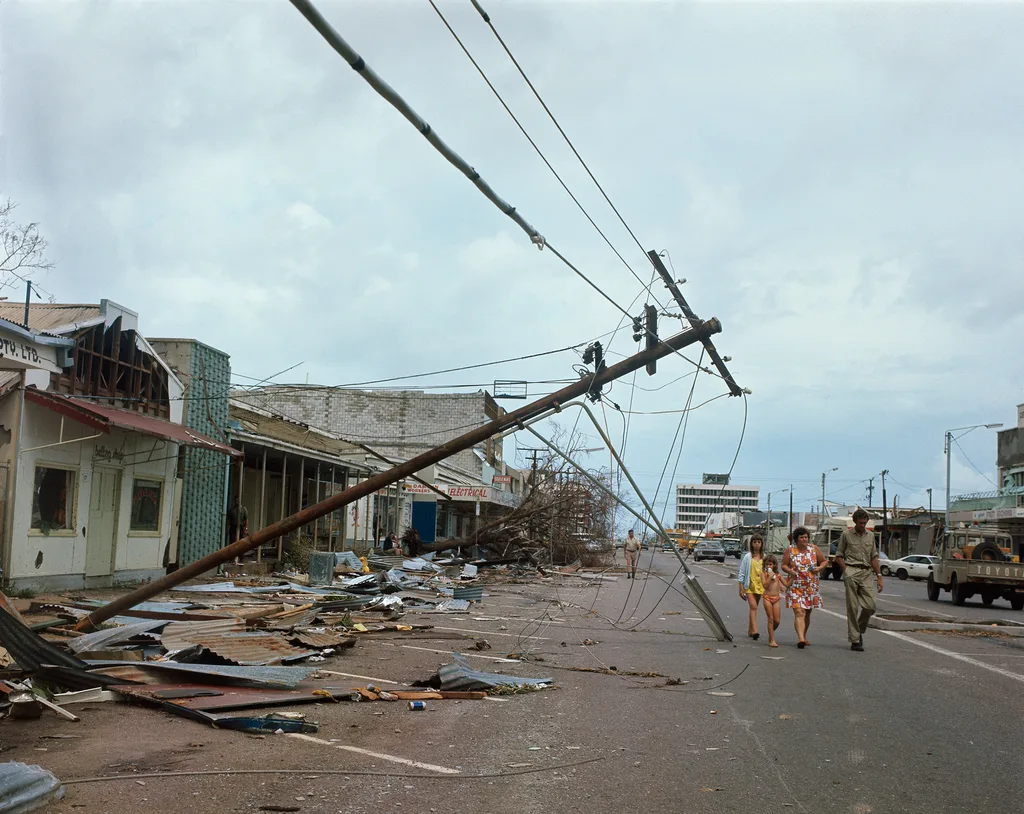 A family walks pasts a fallen telegraph pole and debris from buildings in Darwin after Cyclone Tracy.