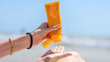 A person squeezing sunscreen into their palm.