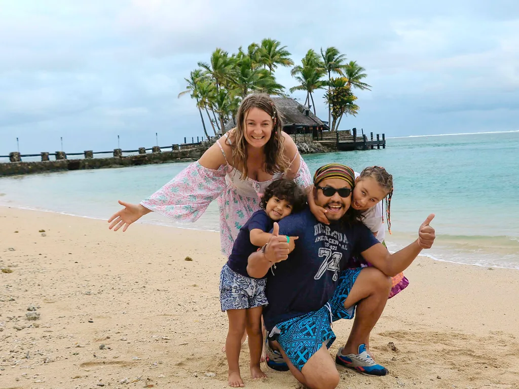 A mum, dad and two kids pose on a tropical beach.