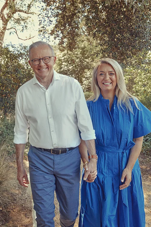 Jodie Hayden dressed in blue dress and Prime Minister Anthony Albanese dressed in navy chinos and white shirt holhold hands