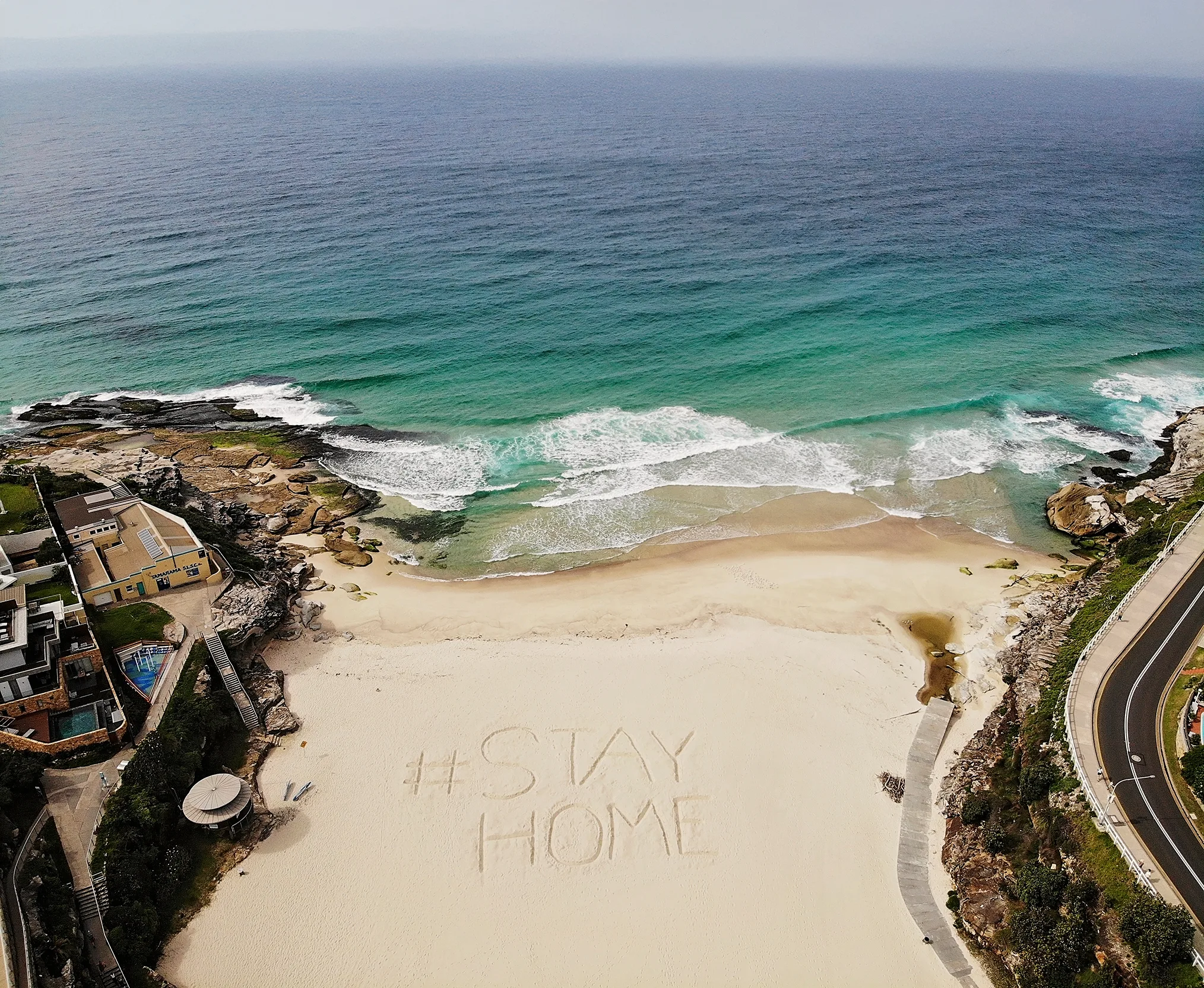 The words #STAY HOME have been engraved into white sand at a beach edged by turquoise water.