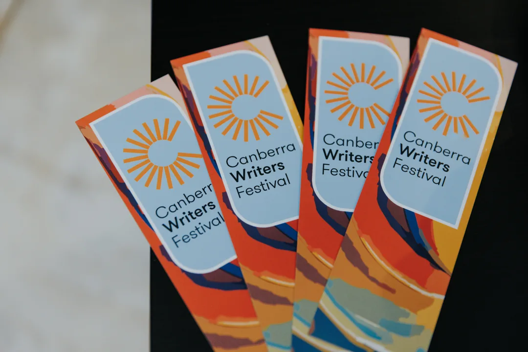 Four bookmarks on a black table that say 'Canberra Writers Festival'