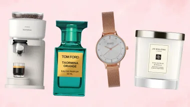 A collection of four lifestyle products - a Philips white espresso machine, a teal bottle of Tom Ford perfume, a rose gold mesh watch, and a Jo Malone scented candle - arranged against a light pink background.