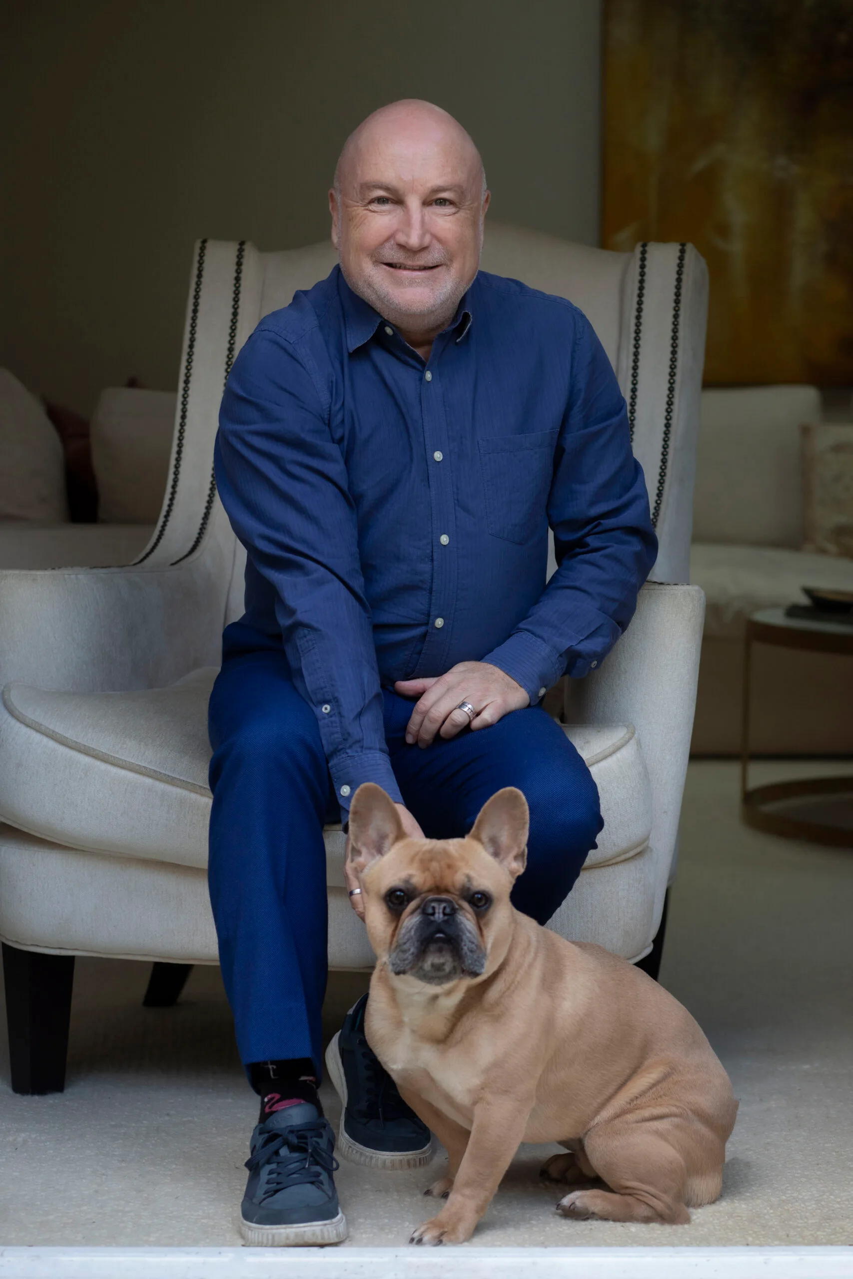 Dr Mark Cross sits on a white armchair and pats a dog.