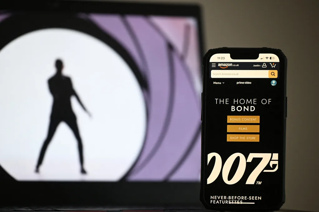 In this photo illustration created in London on February 23, 2025 the Amazon.co.uk app displays "The Home Of Bond" on a phone screen next to an photograph displayed on a laptop screen.