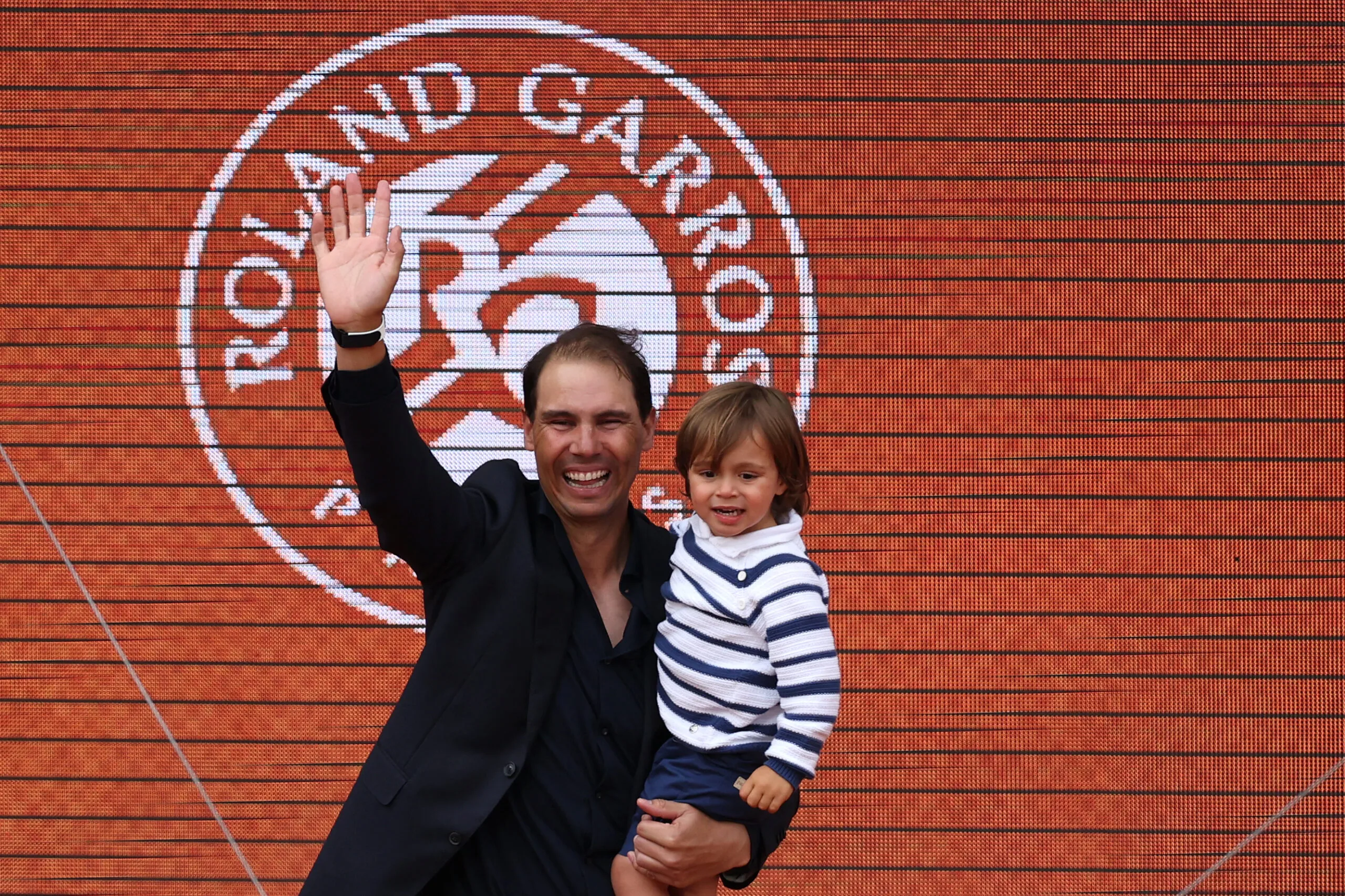 OPSHOT - Former Spanish player Rafael Nadal, with his son Rafa junior in his arms, greets the spectators at the end of a ceremony honoring his career on Court Philippe-Chatrier during the French Open tennis tournament at the Roland-Garros Complex in Paris on May 25, 2025. May 23, 2025, marked 20 years since Spain's Raphael Nadal shook Roland Garros with his first match at the French Open, changing the tennis tournament's history forever. Two decades and 14 titles later, the clay court legend, who retired in November 2024, will receive a tribute during the tournament on May 25, 2025. (Photo by Franck FIFE / AFP) (Photo by FRANCK FIFE/AFP via Getty Images)