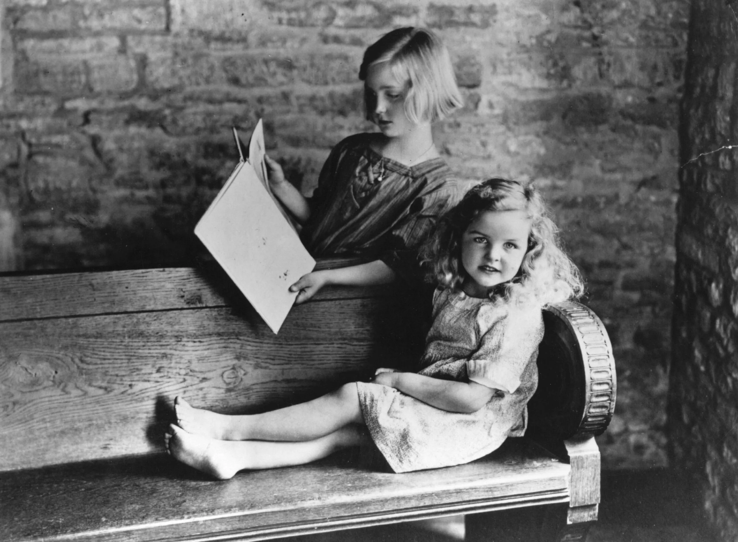 English writer Jessica Mitford, at the age of six, reading with her nine-year-old sister Unity in the garden of their house in Asthall. (Photo by Evening Standard/Getty Images)