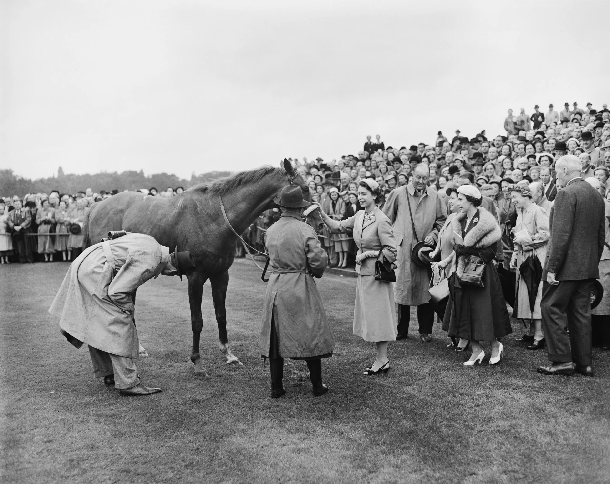 Queen Elizabeth II (1926 - 2022) patting her horse, Auriole, in the paddock after it won the King George VI and Queen Elizabeth Stakes, ridden by Eph Smith, at Ascot Racecourse, Berkshire, 17th July 1954. Princess Margaret (1930 - 2002) and the Queen Mother (1900 - 2002) look on (right). (Photo by Reg Speller/Fox Photos/Hulton Archive/Getty Images)