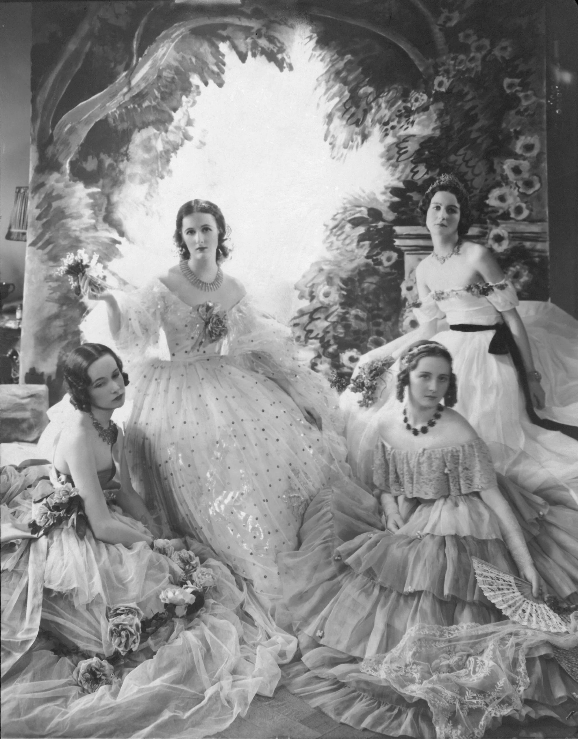 The Famous Beauties Ball in London: Miss Baba Beaton (second from left) surrounded by Jess Chattock, Nancy Mitford, and Carol Prickard in enormous pageant dresses before background painting. (Photo by Cecil Beaton/Condé Nast via Getty Images)