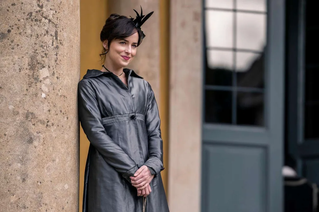 persuasion dakota johnson. a woman stands in front of a sandstone building wearing a grey dress