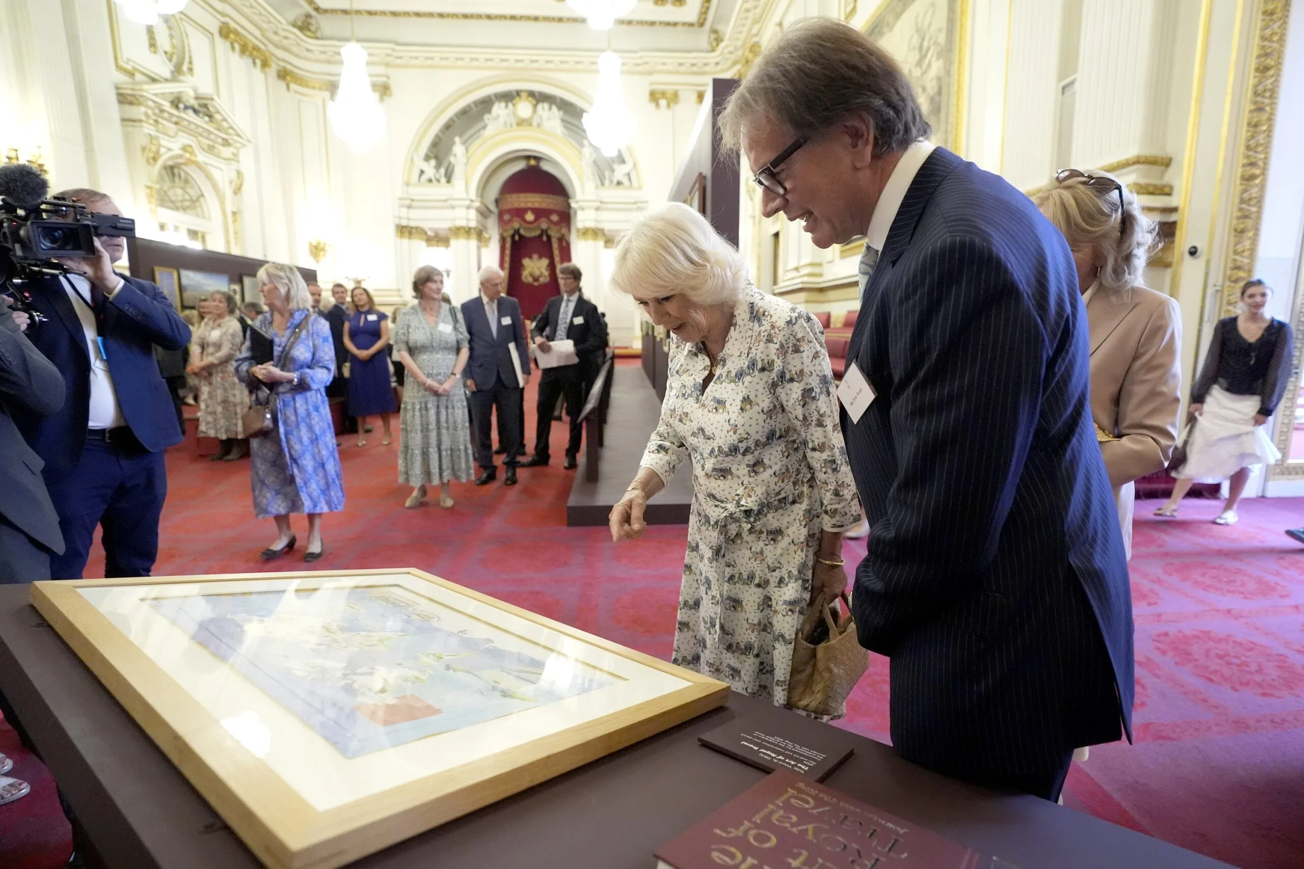LONDON, ENGLAND - JULY 9: Queen Camilla with artist Toby Ward, who was commissioned for the endpapers of the book 'The Art of Royal Travel: Journeys with The King', during a reception for the King's Tour Artists exhibition celebrating 40 years of artists accompanying official overseas visits at Buckingham Palace, on July 9, 2025 in London, England. The exhibition features the work of 43 artists who have joined the King on 70 official visits across 95 countries and regions. (Photo Andrew Matthews - WPA Pool/Getty Images)