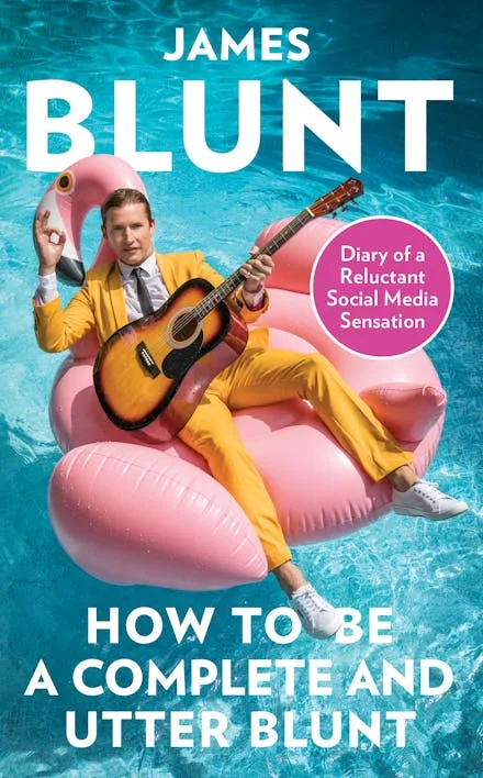 Book cover of How to be a Complete and Utter Blunt. James Blunt sits in a flamingo poo, floaty holding a guitar.