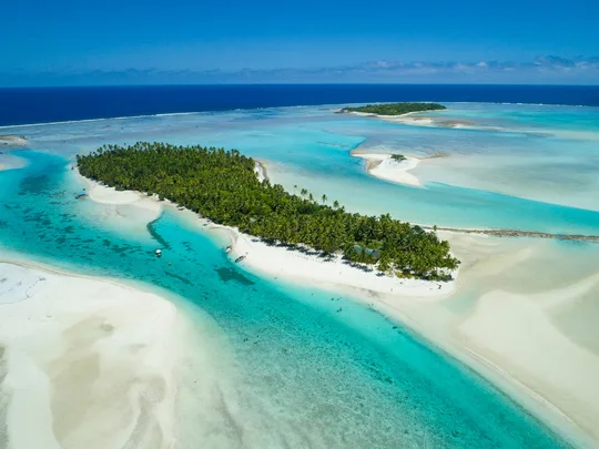 A small palm-covered island with gleaming white sand adorns an atoll.