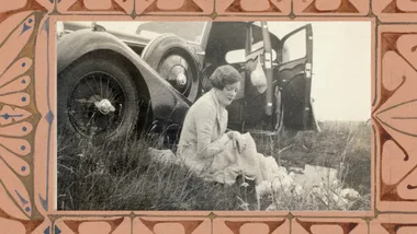 Black and white image of a woman sitting beside a car.