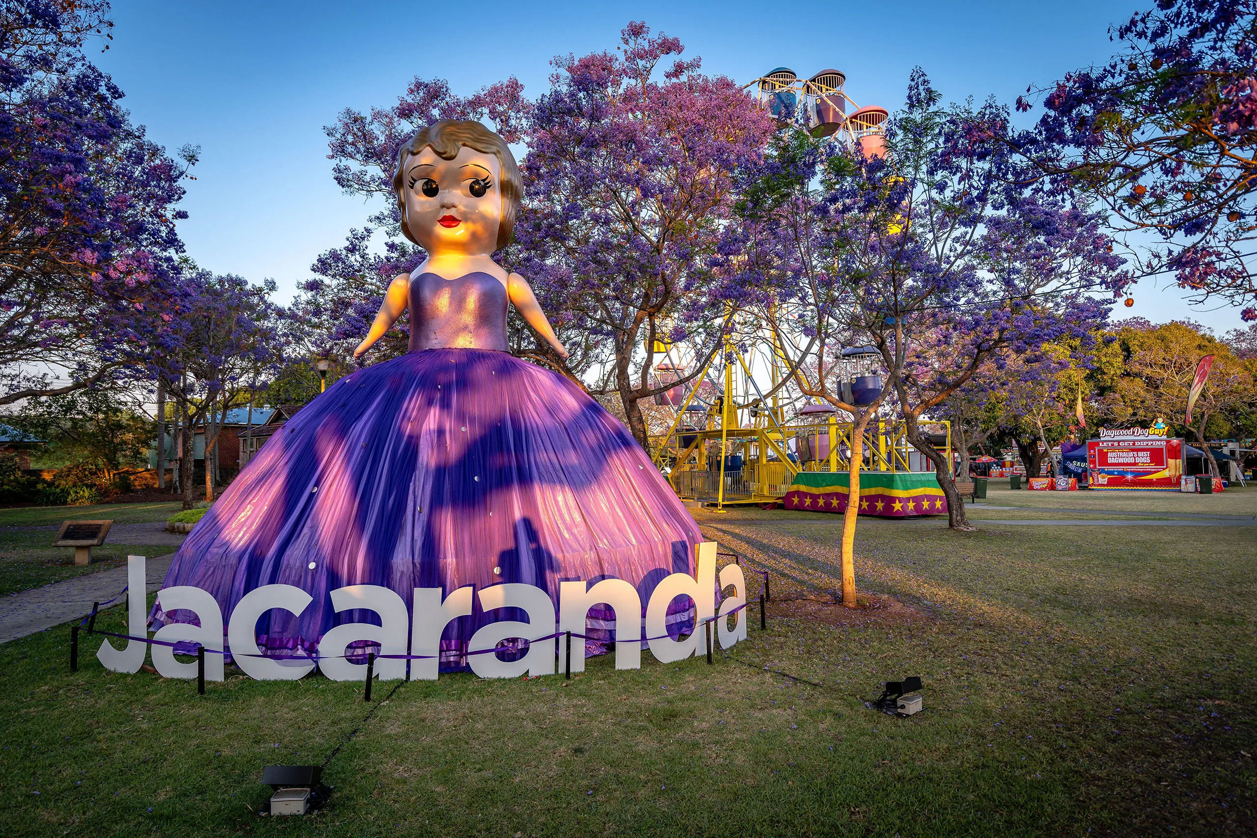 A large doll statue in a purple dress that says 'Jacaranda' at the jacaranda flower festival in Grafton