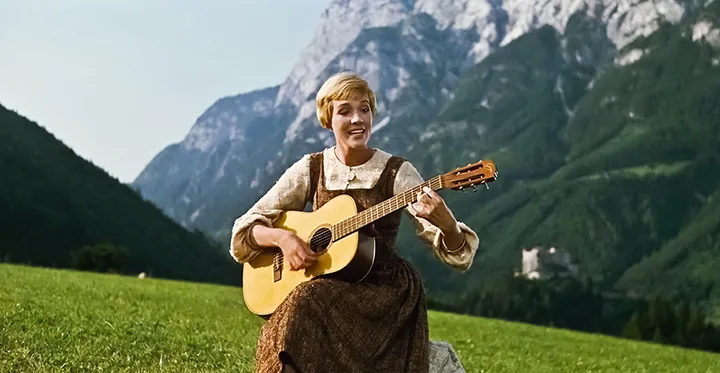 Julie Andrews in The Sound of Music. Playing a guitar and singing on a mountain.