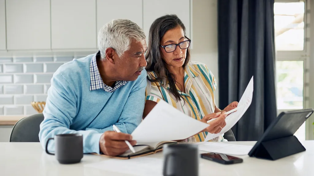 man and woman sit at a kitchen bench looking at printed sheets of paper
