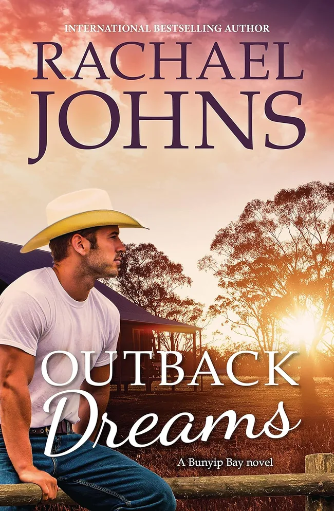 Rachael Johns outback dreams book cover. A man in jeans, white T-shirt and cowboy hat sits on a wooden fence in front of a farm house.