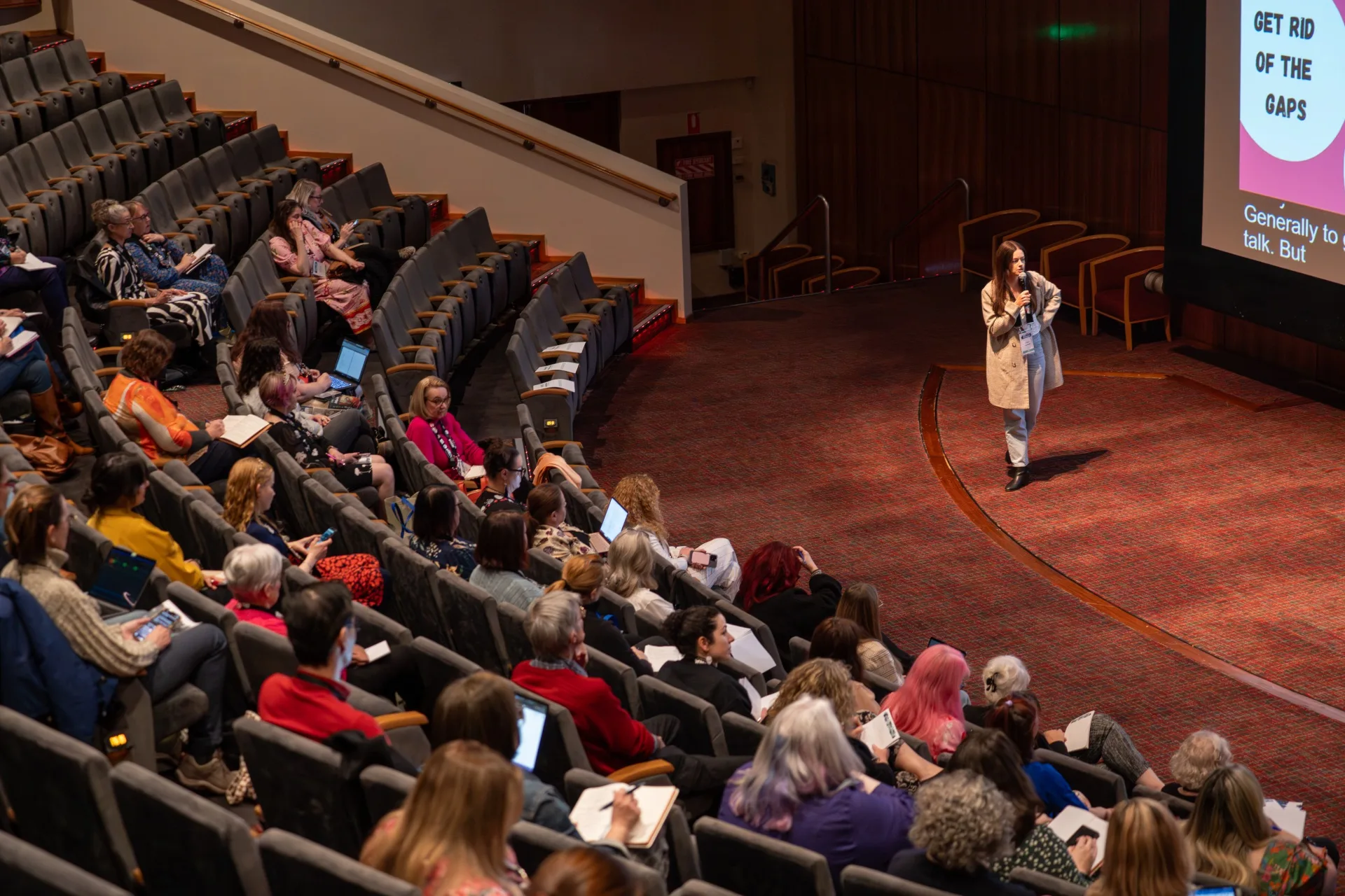 People sitting in an auditorium watching a woman speaking.