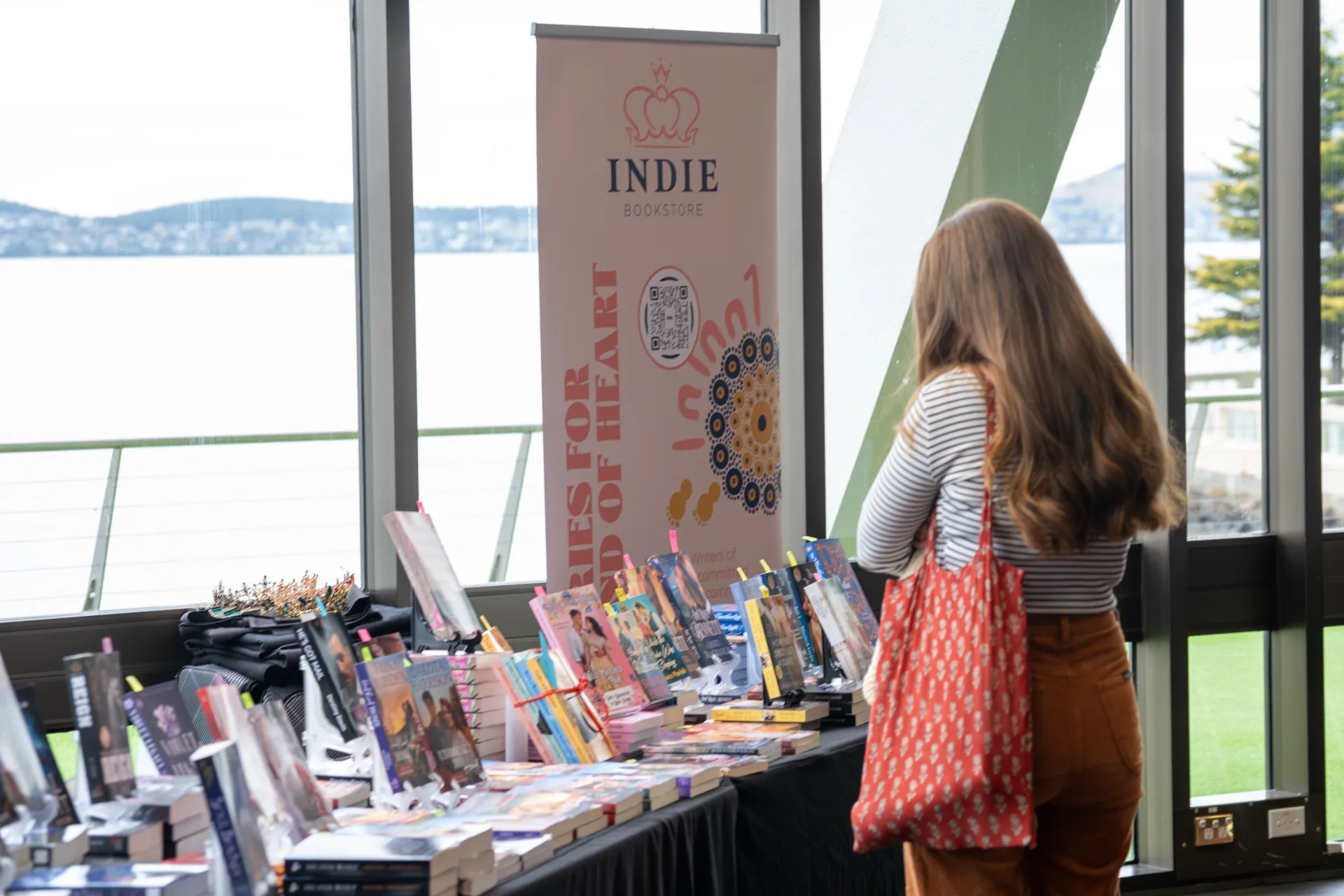 A woman with long brown hair stands in front of a table displaying books.