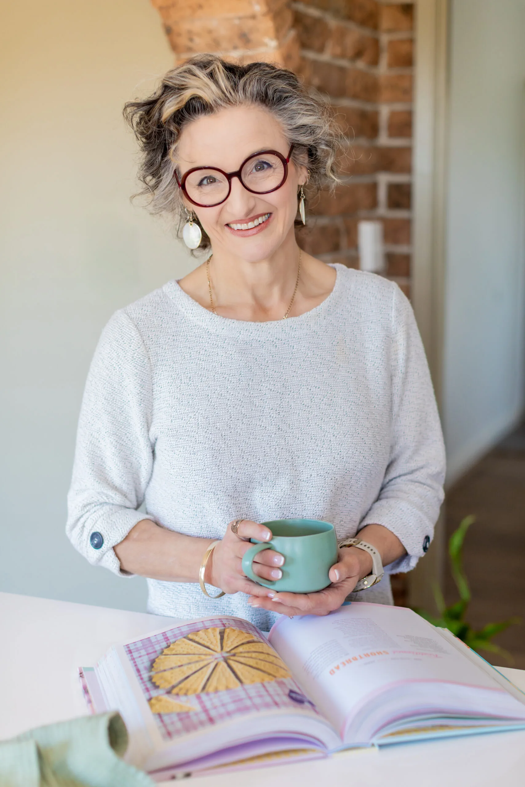 Julie Goodwin holdign a cup of tea with her cookbook. Photo by Leah Stanistreet