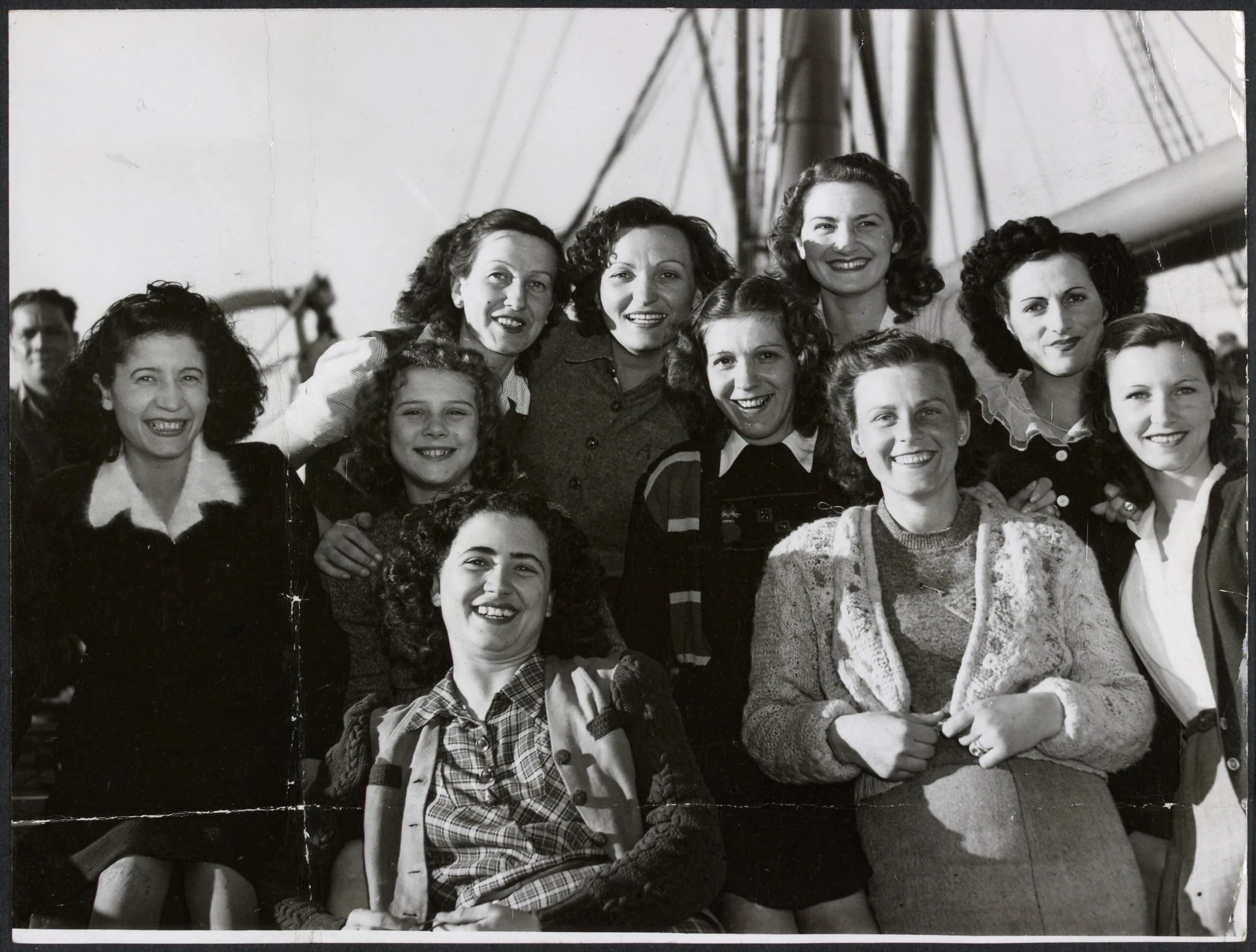 Ten smiling women in 1940s-style hair and clothing cluster together for a group photo.