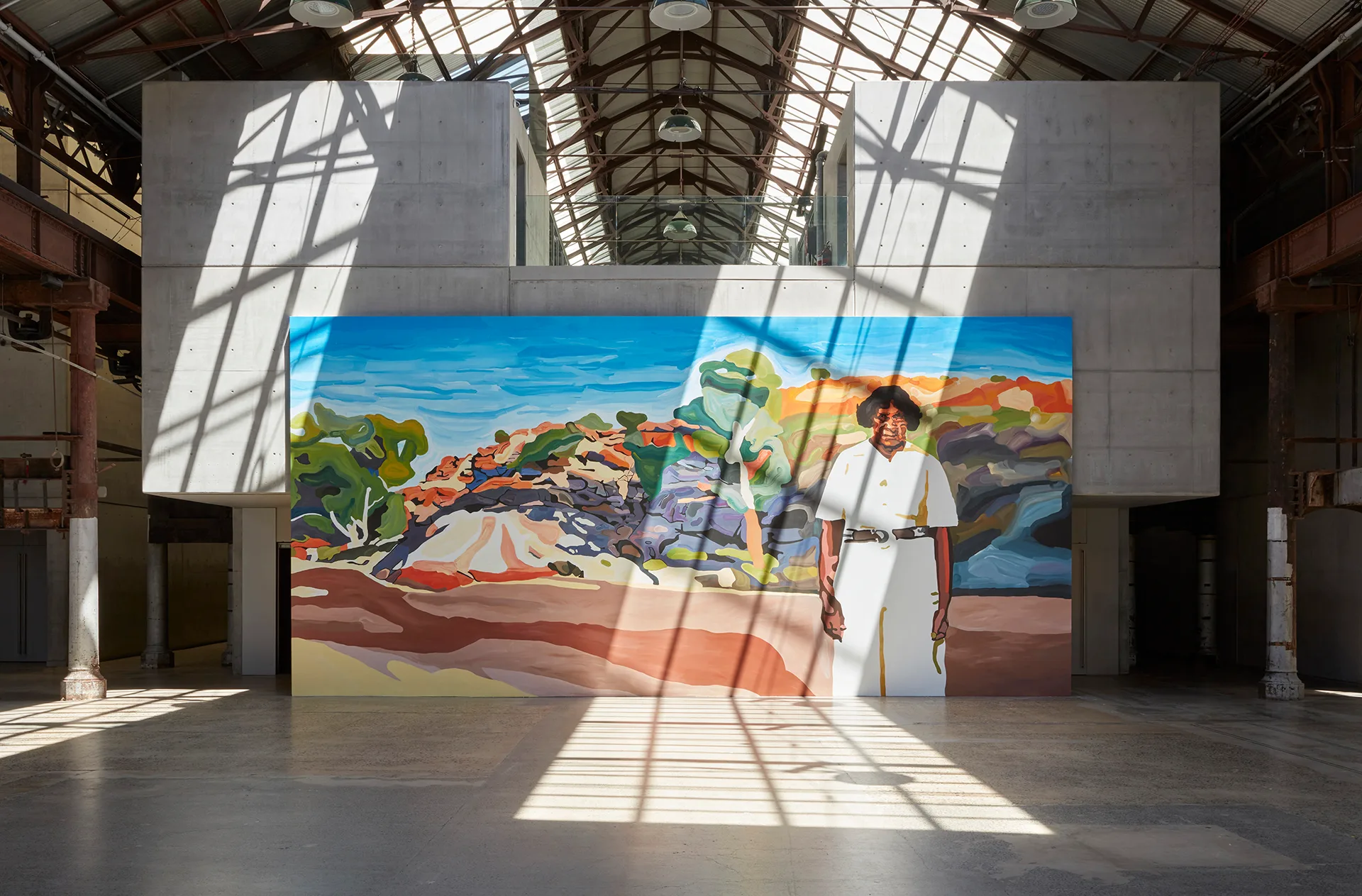 A very large painting of Hetty Perkins standing in a Central Australian landscape. The painting is enormous and is photographed in situ at the Carriageworks where it takes up almost an entire wall.