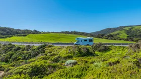 Campervan hire driving on a scenic road against a backdrop of lush green landscape and bright blue sky, perfect for an Australian road trip for over 50s.