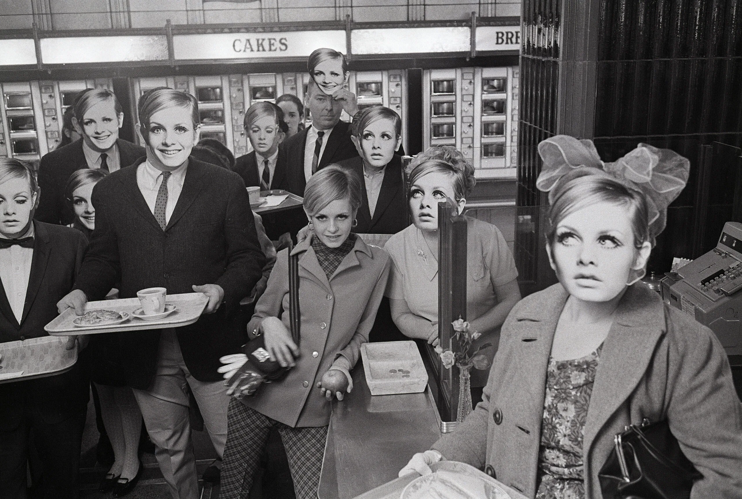 Fashion model Twiggy poses in an automat cafeteria, surrounded by regular people wearing masks of her face in New York.