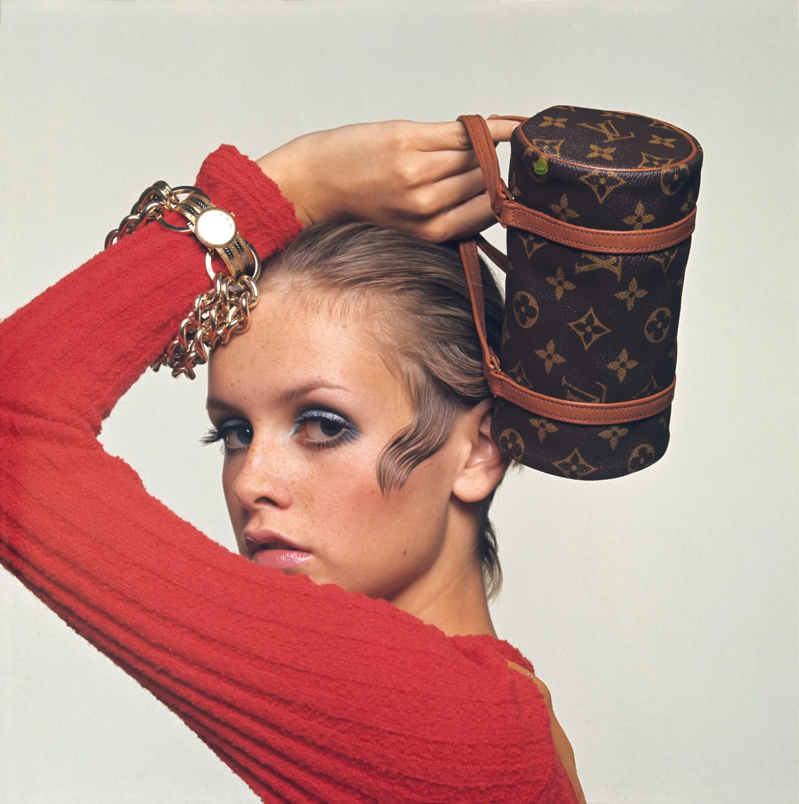 Model Twiggy wears a wool chenile Pattie Tuttman for Silverworm jumpsuit and holds a Louis Vuitton roll bag made of Vuitton canvas; Oster for Paraphernalia chain bracelet and a Vacheron Constantin watch. (Photo by Bert Stern/Cond&eacute; Nast via Getty Images)
