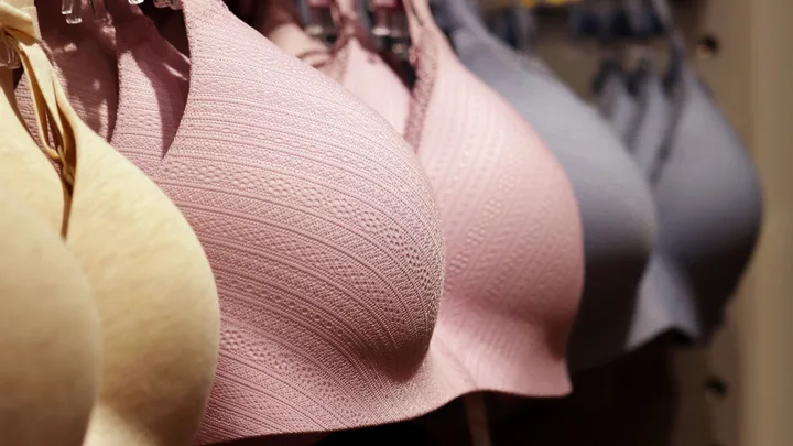 Close-up of beige, pink and blue bras hanging on a rack, with focus on the textured pink bra in the centre.