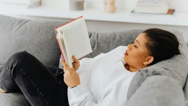 black woman reading a book while lying on a couch