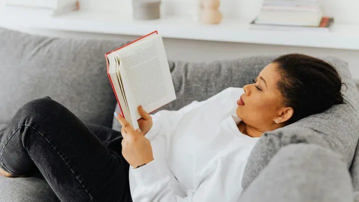 black woman reading a book while lying on a couch