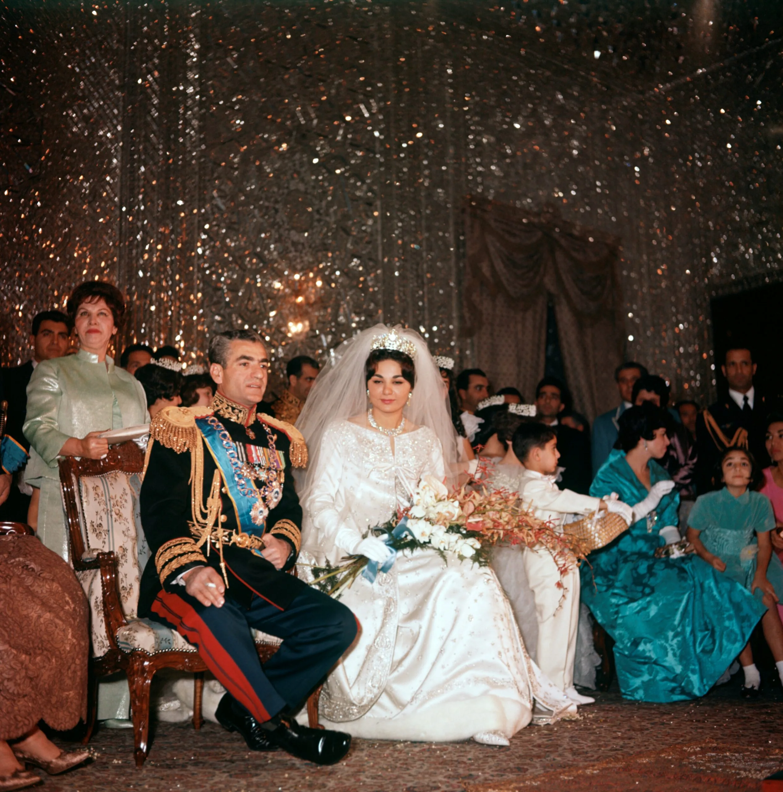 Mohammad Reza Pahlavi, Shah of Iran, is seated next to his third wife Farah Diba on the day of their marriage; her gown is by Yves St Laurent and on her head a Noor-ol-Ain Diamond tiara. Iran, 21st December 1959. (Photo by Mondadori Portfolio by Getty Images)