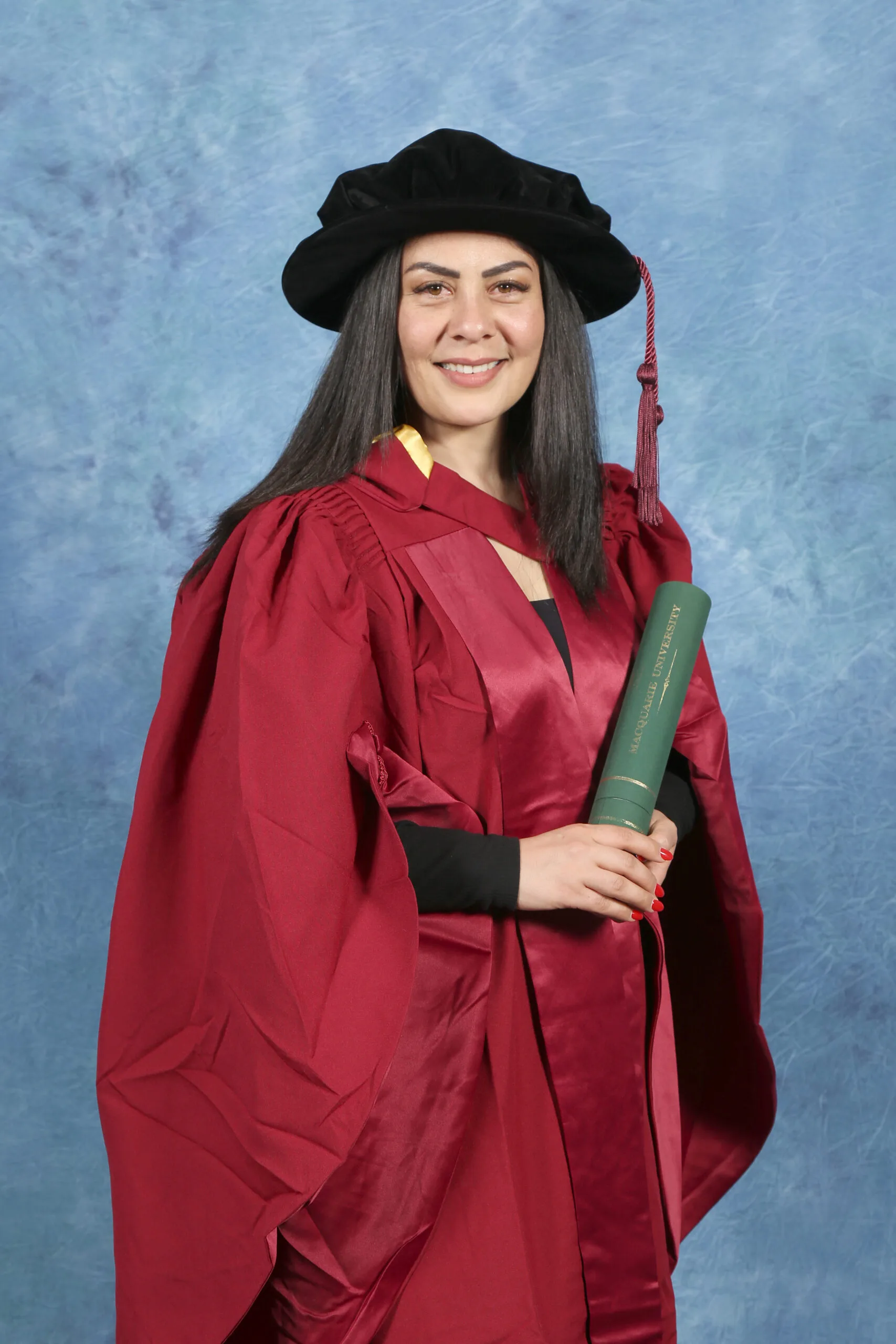 Saba wears a red academic gown and  cap as she collects her PhD.