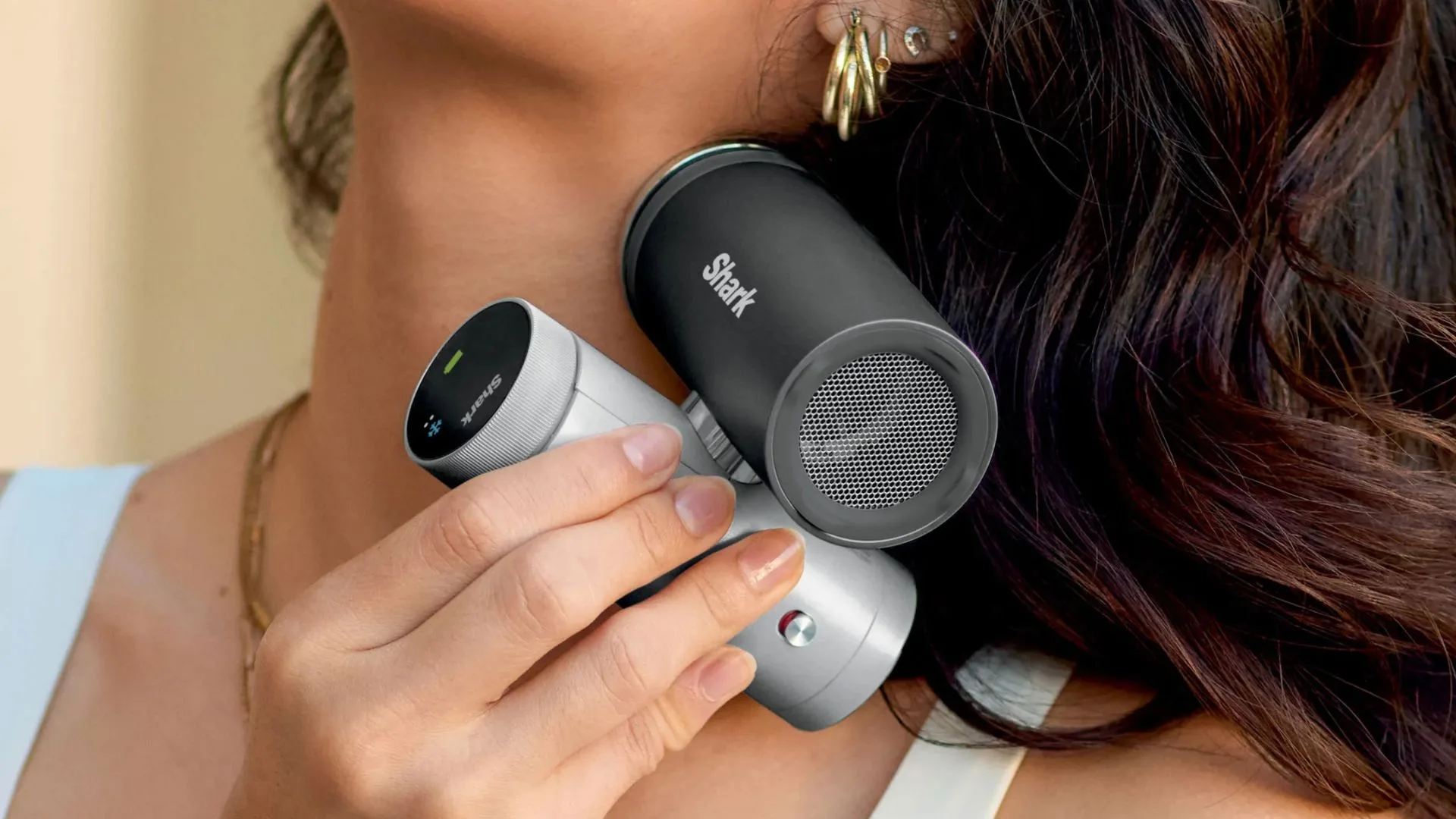 A close-up shot of a person holding the Shark ChillPill, a compact, pill-shaped portable cooling device, against the side of their neck. The device features a sleek two-tone design with a black upper section displaying the "Shark" logo and a silver lower section with a digital display and control buttons. Appearing in the article for best personal cooling fans Australia