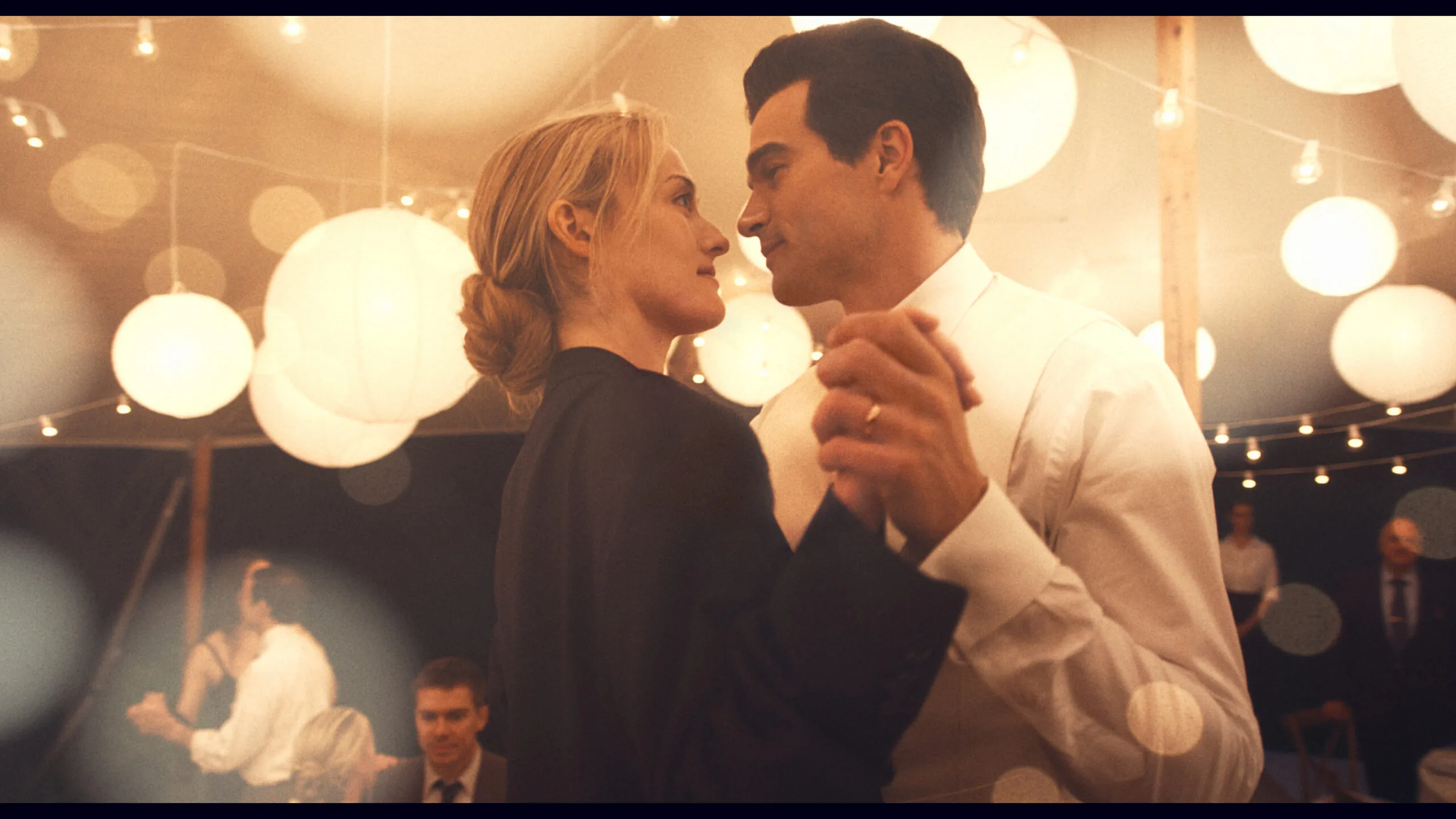 Sarah Pidgeon, her blond hair in a low bun, and Paul Kelly, in white dinner shirt, look into each other's eyes as they dance.
