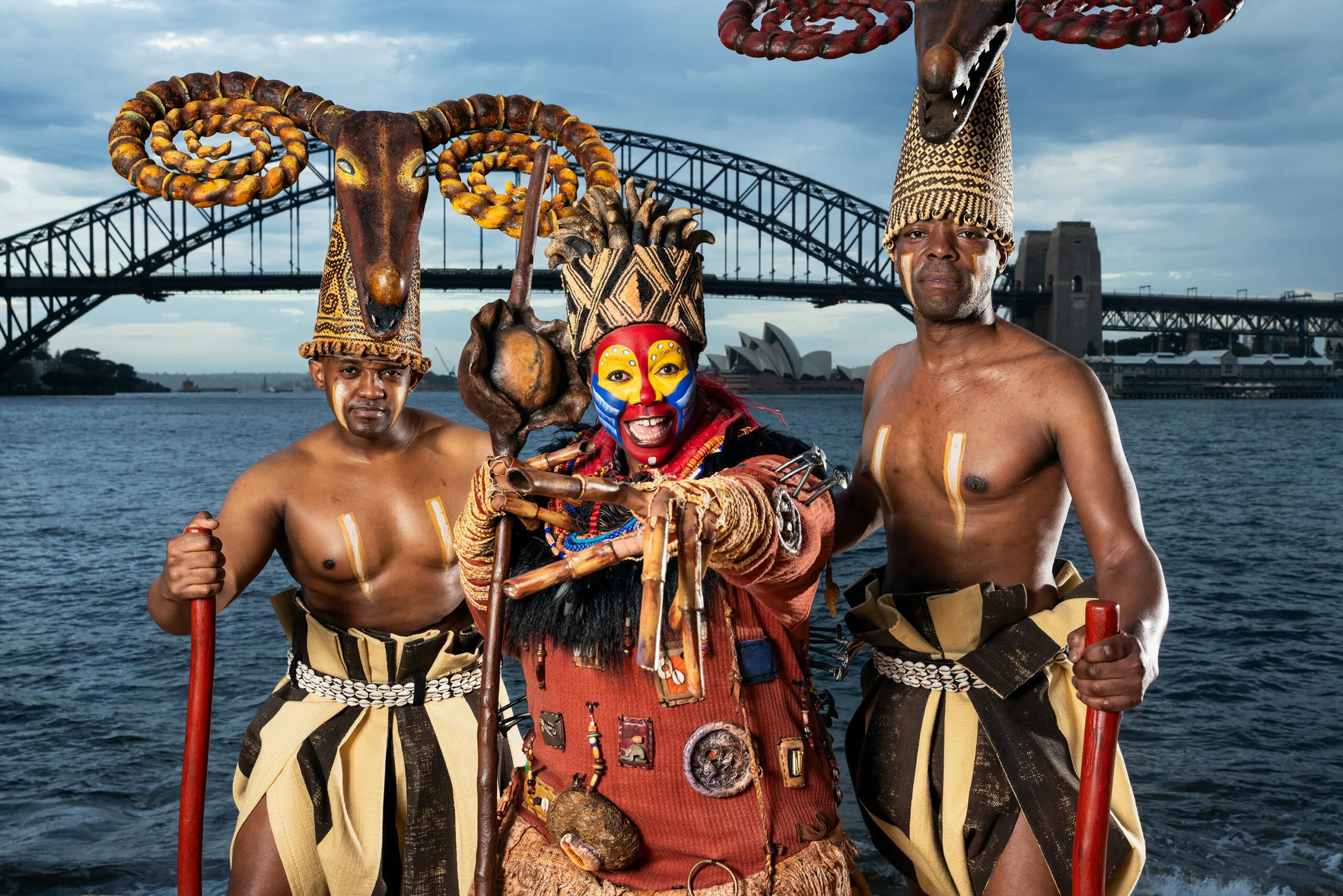 Buyi, with two other cast members, all dressed in full Lion King costumes, stands by the harbour, in front of the Sydney Harbour Bridge.