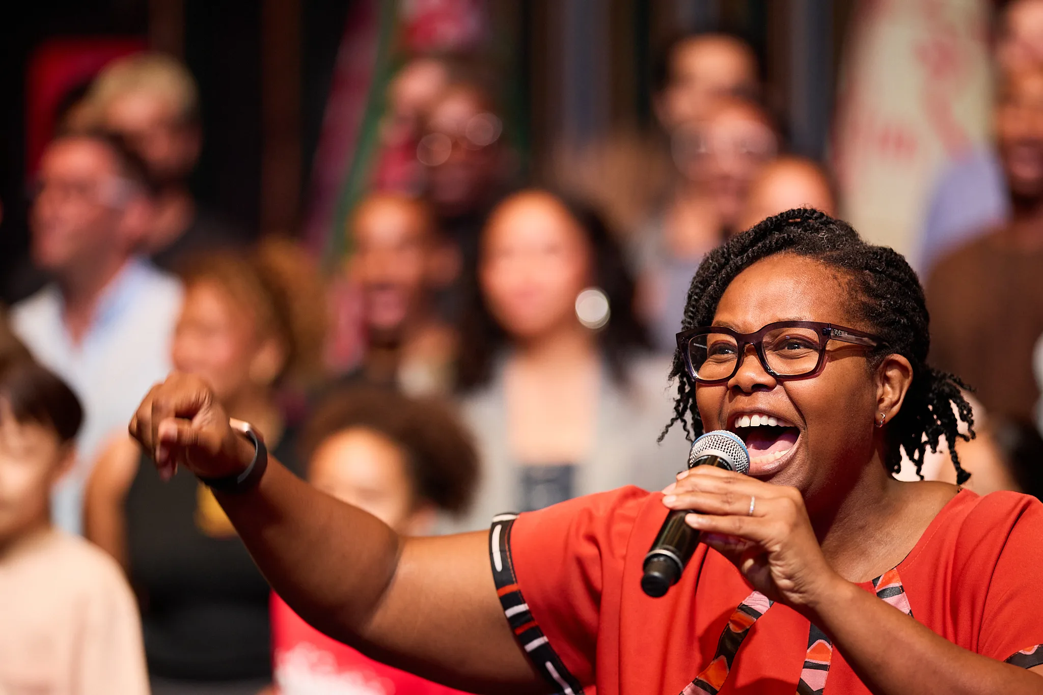 Buyi Zama, wearing a red dress with African print trim is singing into a microphone,