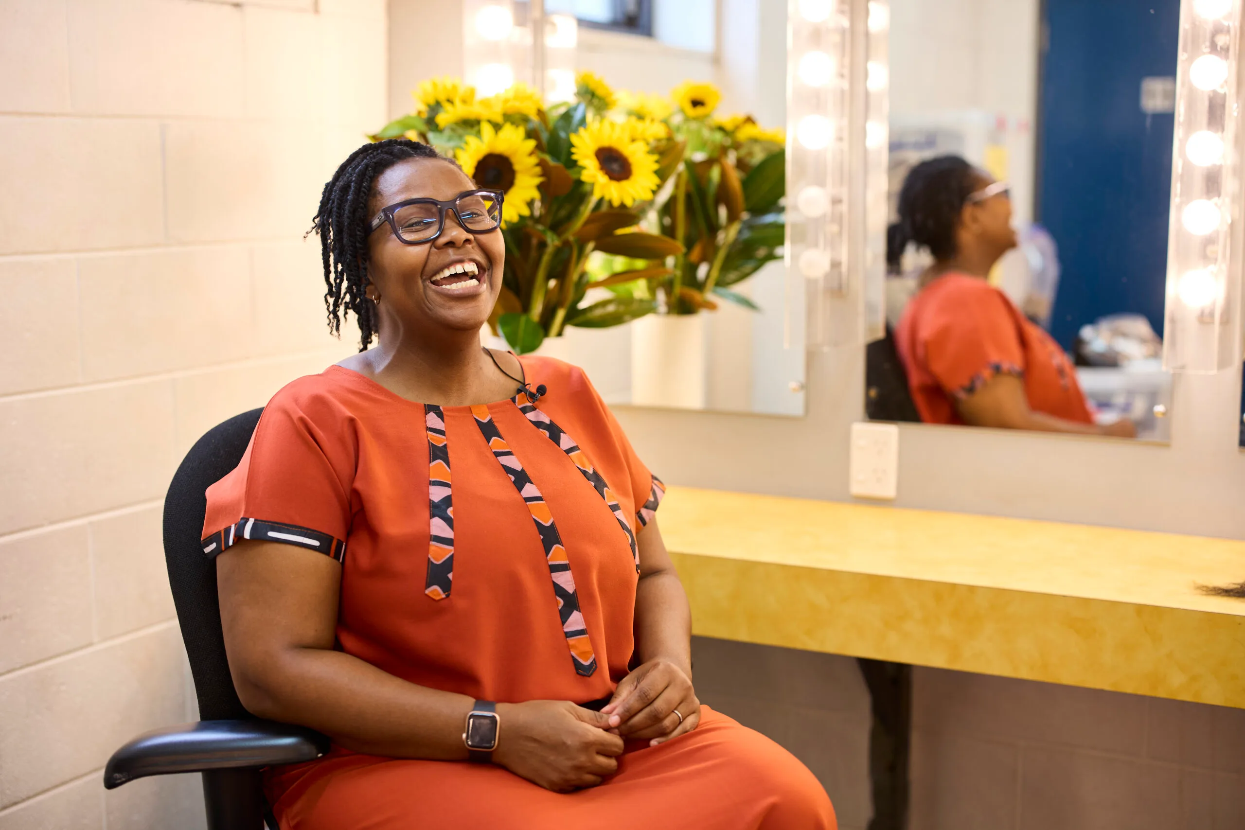 Buyi is seated in a backstage dressing room. A bunch of sunflowers is behind her.